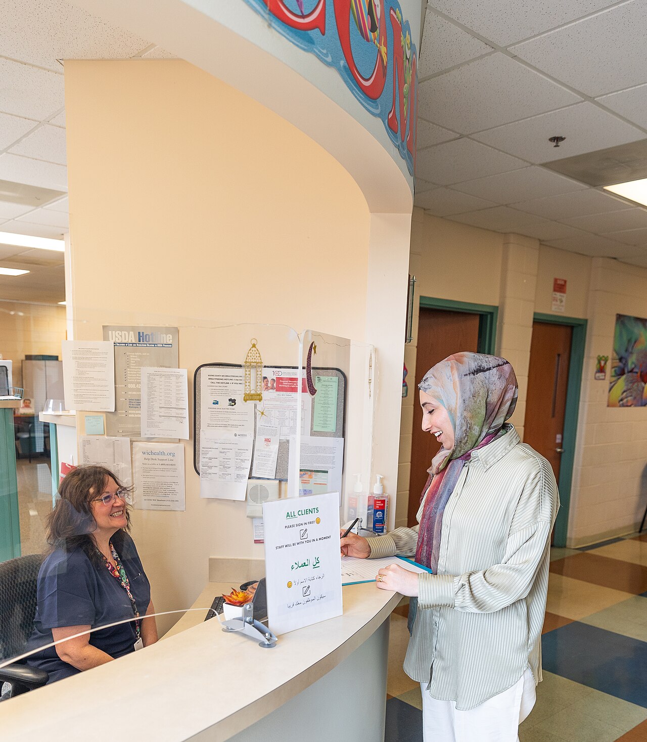 Clinic front desk with a patient signing in while staff handle intake work.